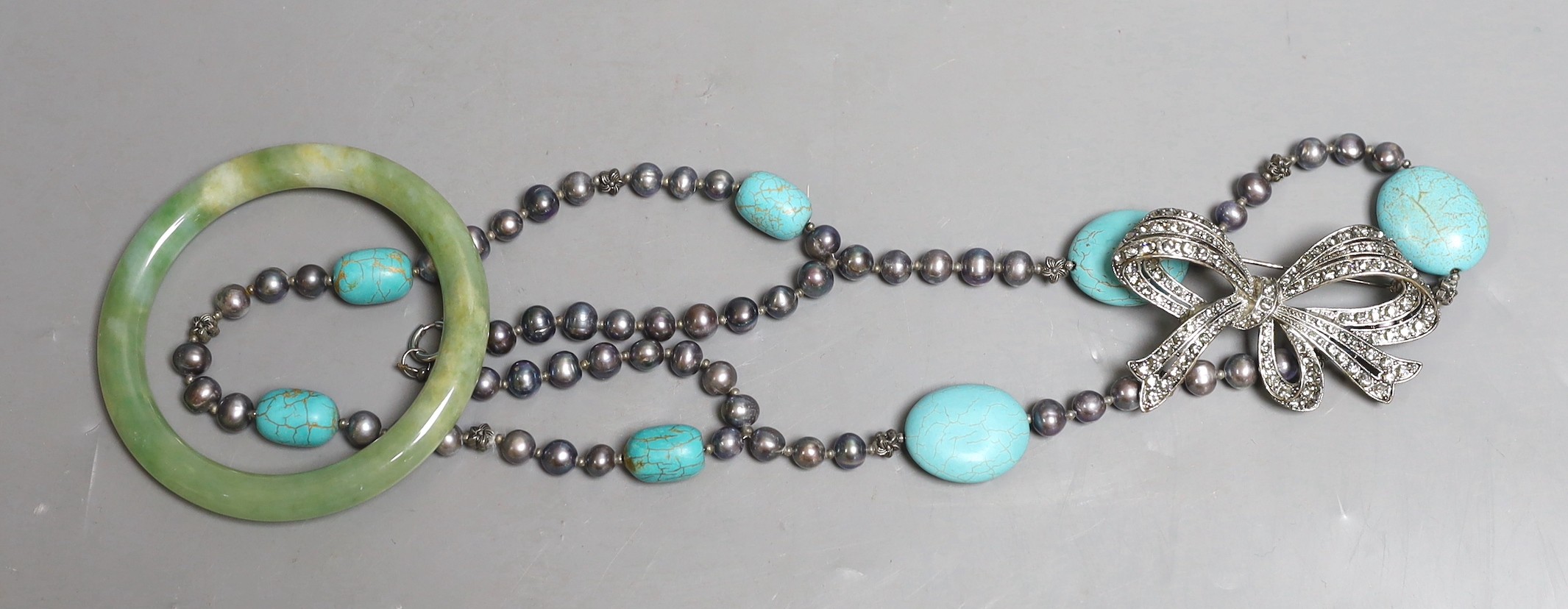 A white metal and paste set bow brooch, a green hardstone bangle and a Tahitian cultured pearl and turquoise set necklace.